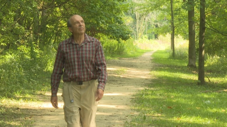 A man walking on a trail surrounded by trees on a summer day.