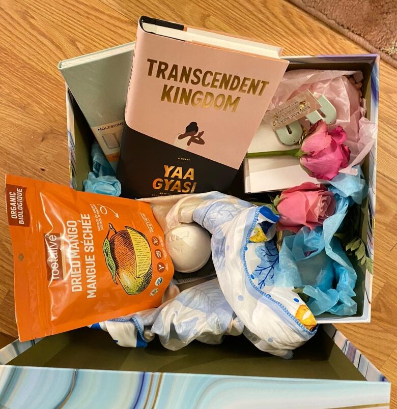 A box overflowing with items includes a bag of dried mangos, several books and a handful of items prettily wrapped in tissue paper. 