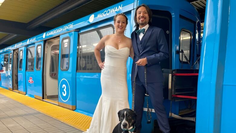 A man and woman in wedding attire stand near a subway car.