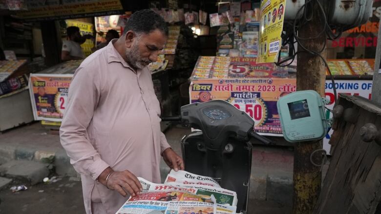 A man looks through some newspapers piled on the seat of a scooter.