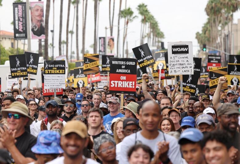 A crowd of people are seen on a street carrying picket signs.