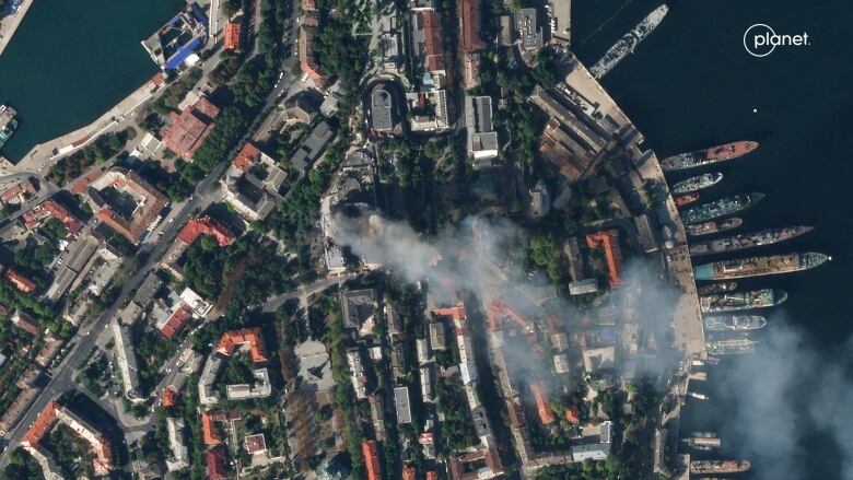 An aerial view of smoke rising from a building surrounded by trees and other buildings.