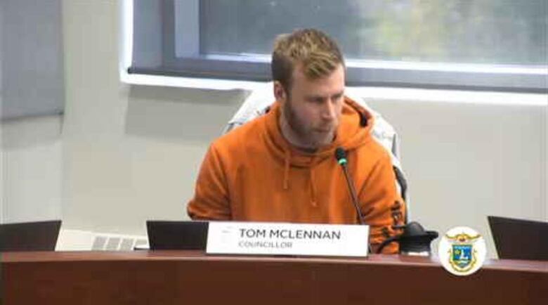 Man in orange hoodie speaking into mic.