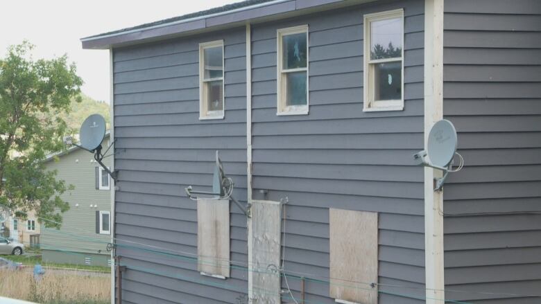 A blue house has wooden boards on the windows.