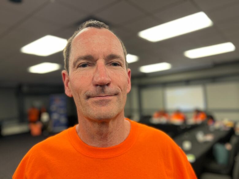 A man in an orange t-shirt stands in a large meeting room.