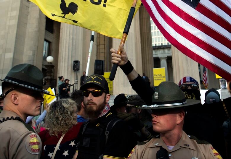 Members of the Proud Boys stand behind Tennessee State Troopers at a rally against gender affirming care at War Memorial Plaza in Nashville, Tenn., Friday, Oct. 21, 2022. Top Tennessee Republicans on Friday vowed to push for some of the strictest anti-transgender policies in the United States at a rally Friday, where hundreds of people cheered in support as LGBTQ rights activists yelled back in protest. (Nicole Hester/The Tennessean via AP)