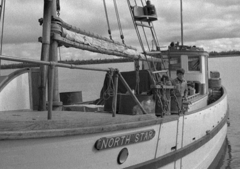 A black and white photo of a young boy standing on board a docked boat that's named 'North Star.'