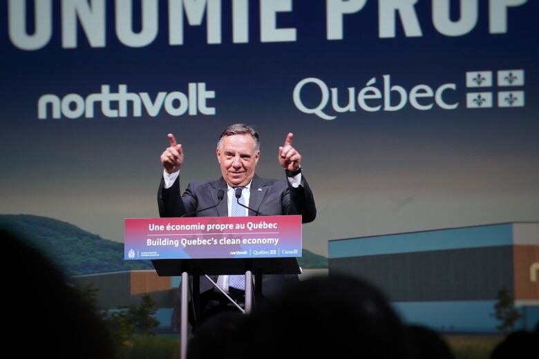 Politician stands at podium with arms raised.