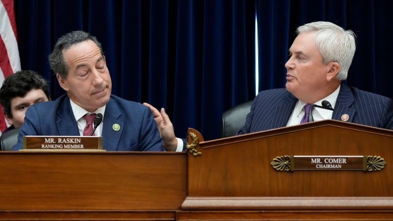 Two men in a suit and tie communicate with each other while seated on a panel table.