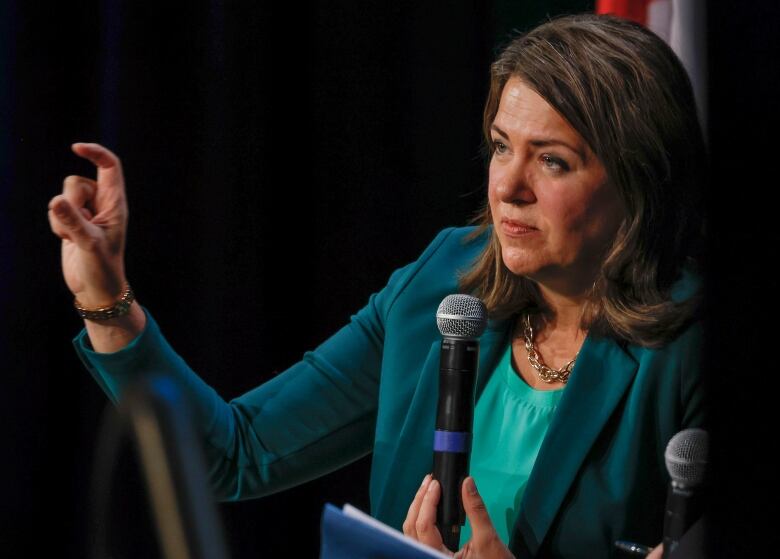 A woman in a green blazer makes a gesture.