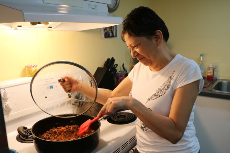 A woman stirs a pot of meat and vegetables on a stovetop.