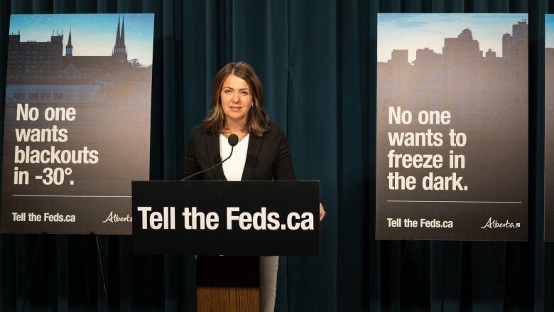 A woman speaks at a lectern, flanked by signs warning of blackouts.