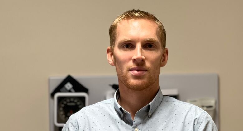 A man stands in front of medical equipment wearing a collared shirt. 