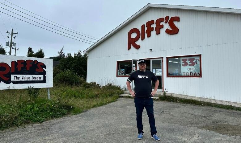 A man dressed in black, with a black hat, stands with his hands on his hips outside a Riff's Department Store.