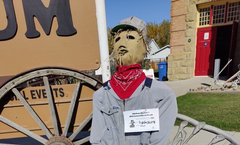 A scarecrow in a train conductor's outfit sits on a bench. 