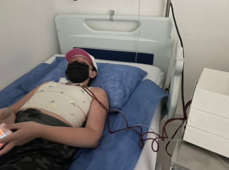 A teenage girl lies on a hospital bed with a mask.