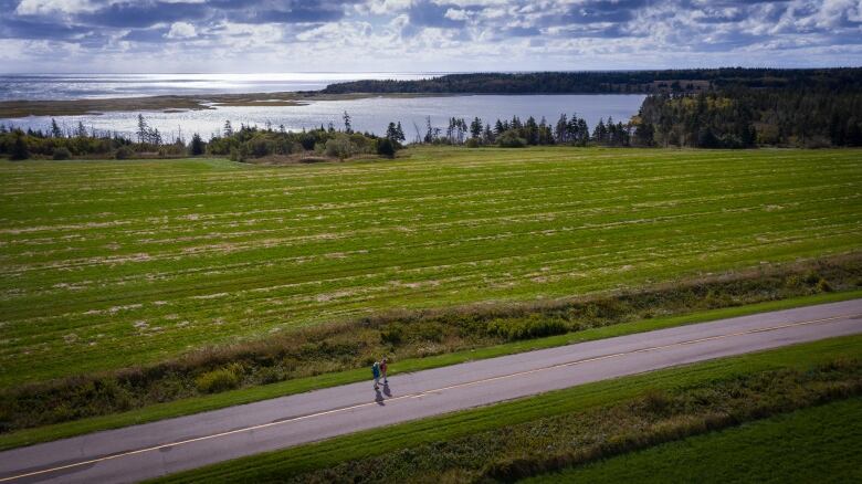 A road bordered by forest and fields in East Point Island, P.E.I. Two people are seen walking along the road.  