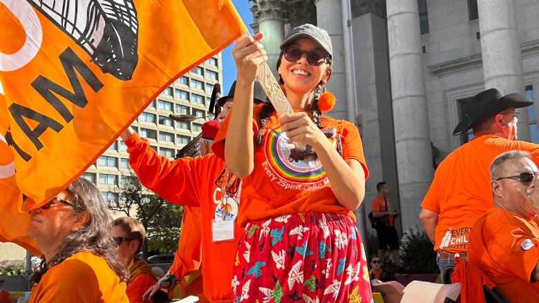 A person in an orange shirt is smiling and waving an orange flag.