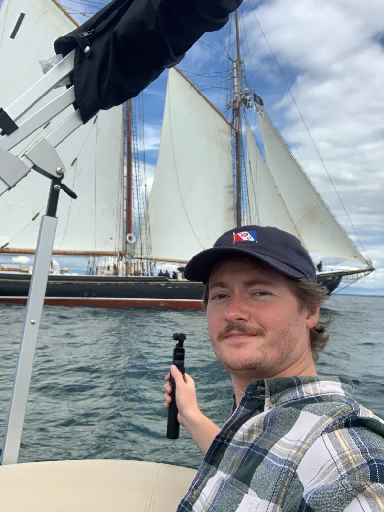 A man with a baseball cap is shooting video of the schooner Bluenose II