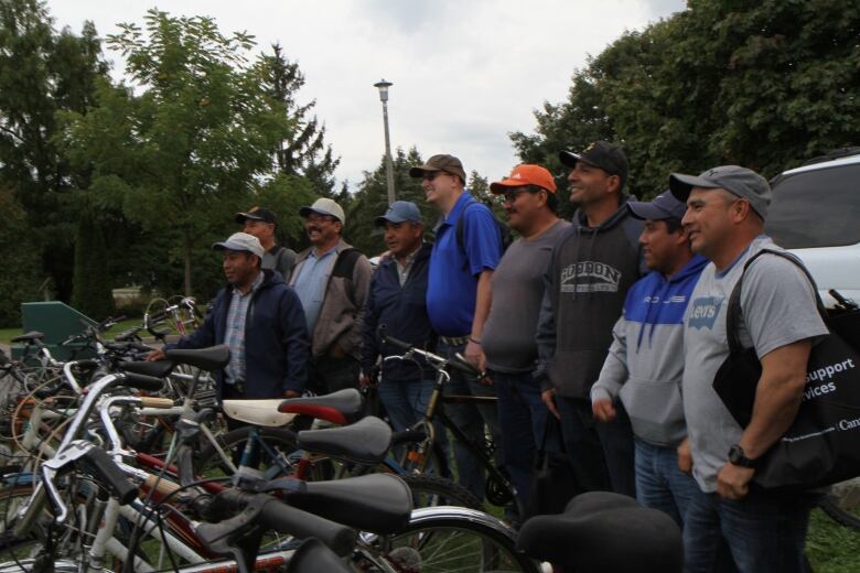 Nine men posing for a photo behind a number of bycicles.