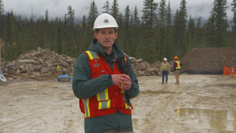 Joshua Kummerfield, a project manager for Parks Canada, stands on a job site in Jasper. He wears a white hard hat, green coat and reflective vest.