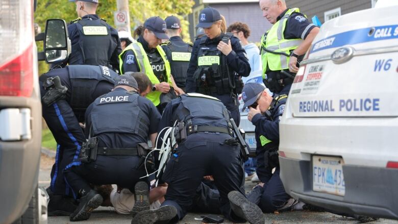 A group of police pin a man on the ground while they attempt to handcuff him.