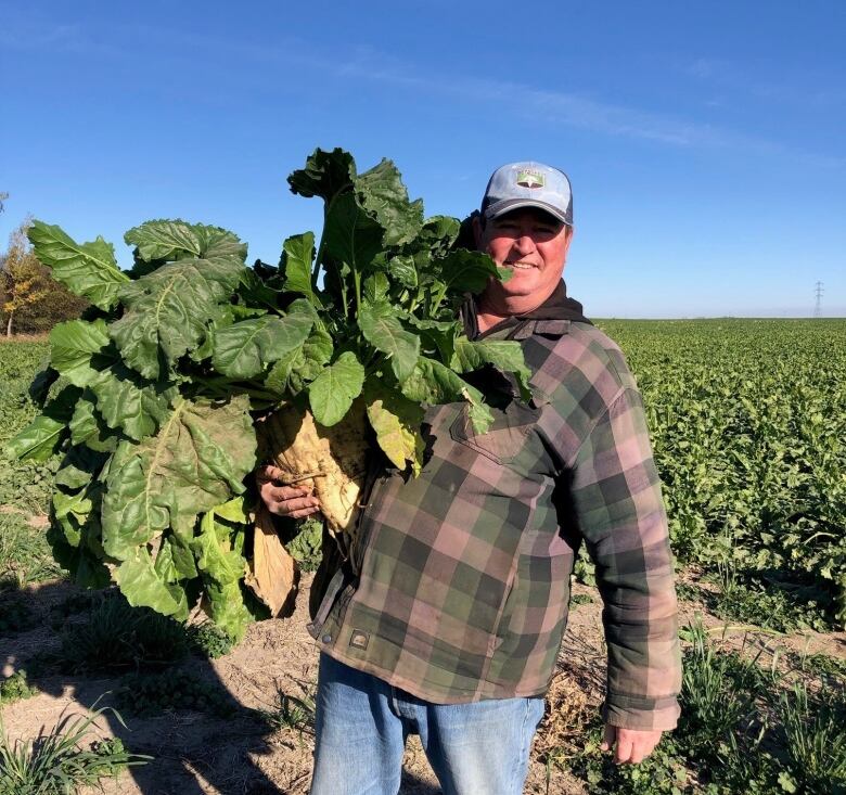 A man stands in a field with a cap on holding vegetables.