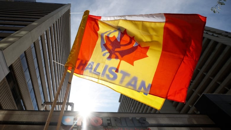 A Canadian flag and a yellow flag with blue lettering that says Khalistan are flown in front of a storefront on a downtown Toronto street.