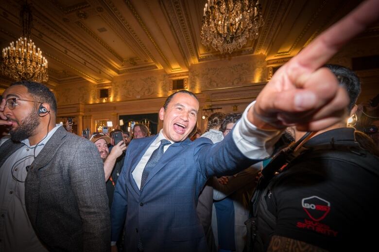 A man points into a crowd with a big smile.