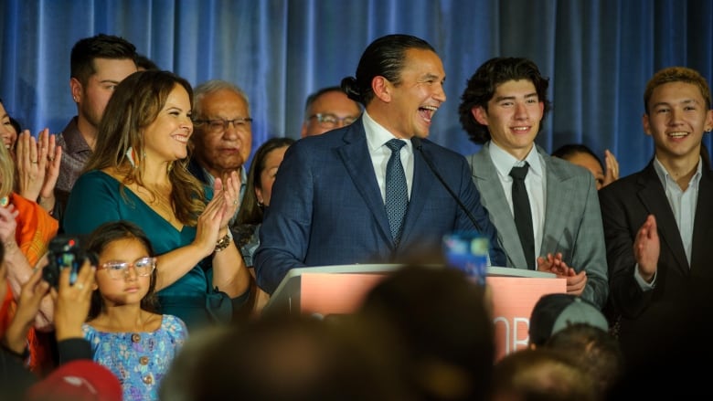 A man speaks at a podium, with supporters around him.