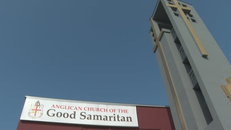 A large gold cross decorates a tower which juts from a large red building. 