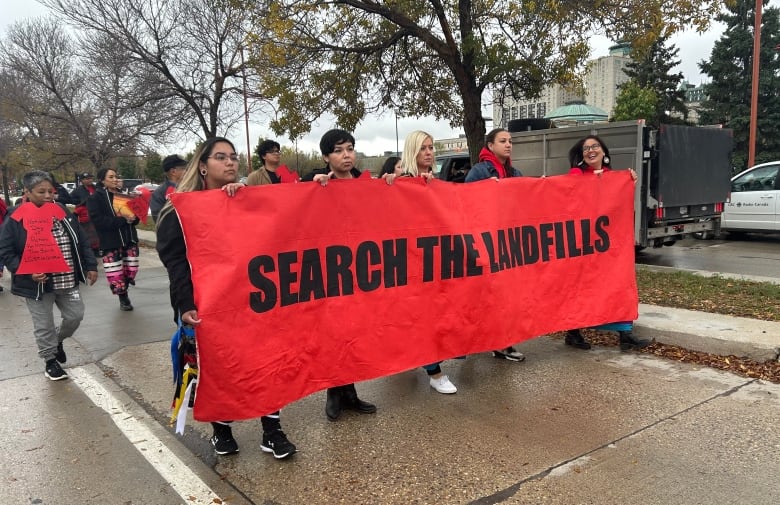 Five marchers carry a large red banner that says 