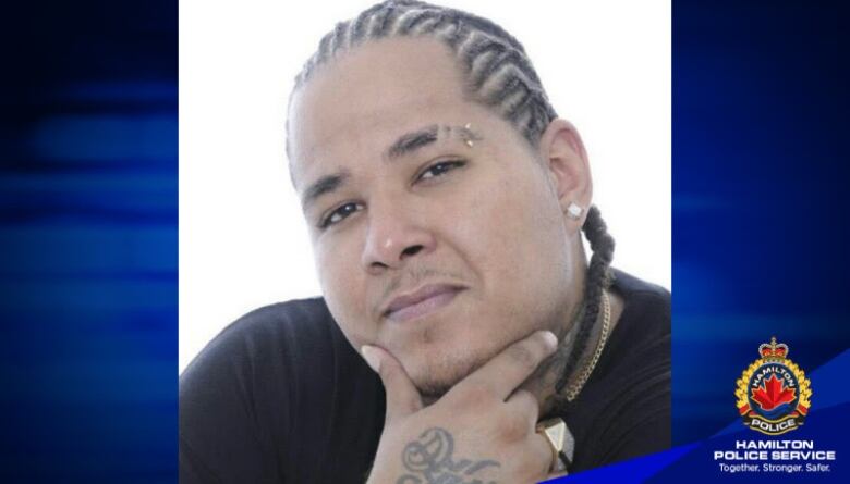 A portrait of a man with cornrows posing with his hand on his chin. There is a Hamilton police Service watermark on the image. 