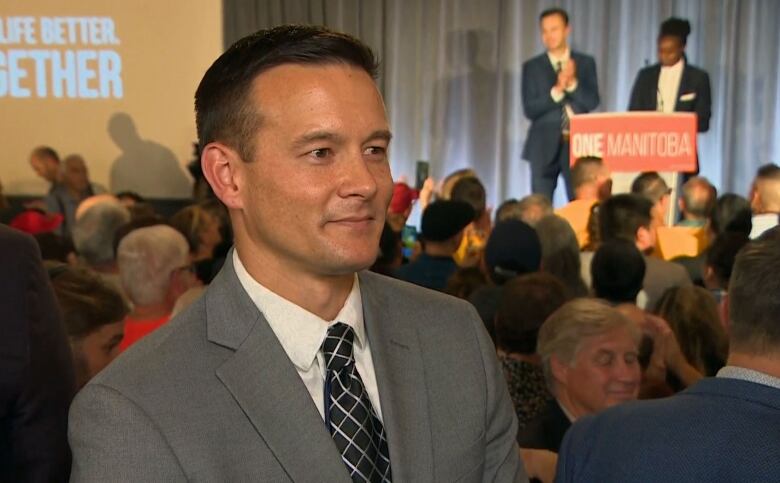 A man wearing a grey suit speaks to a reporter off camera. 