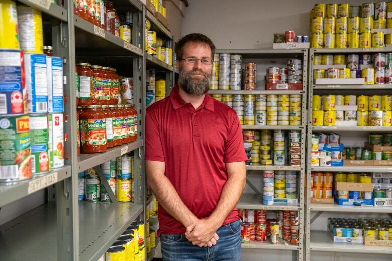 A man wearing a red polo shirt stands in front of shelves of canned goods.