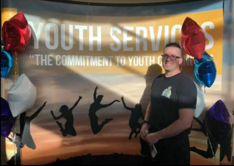 A man wearing an RCMP t-shirt smiles in front of a youth services banner.