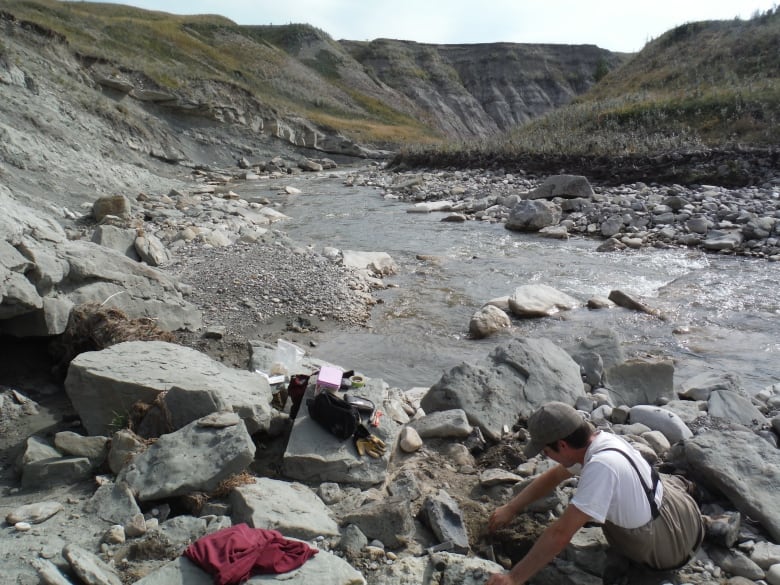 a man sits on the rocks by a stream to search for fossils