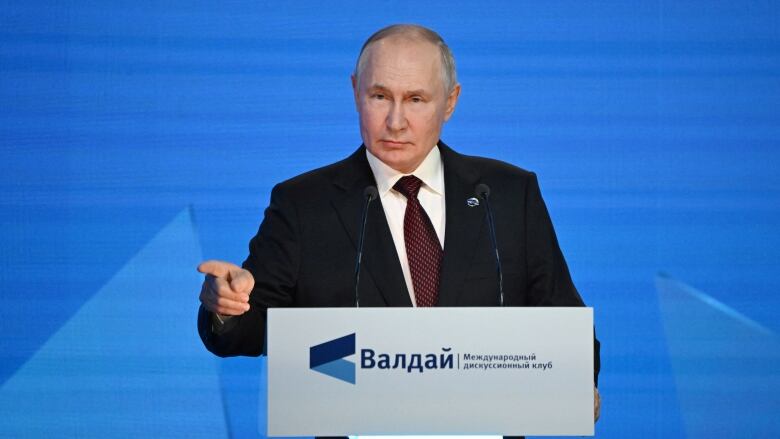 A man points while speaking at a lectern. 