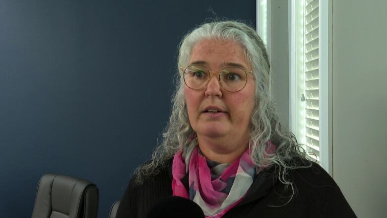 A woman with long grey hair stands in a boardroom.