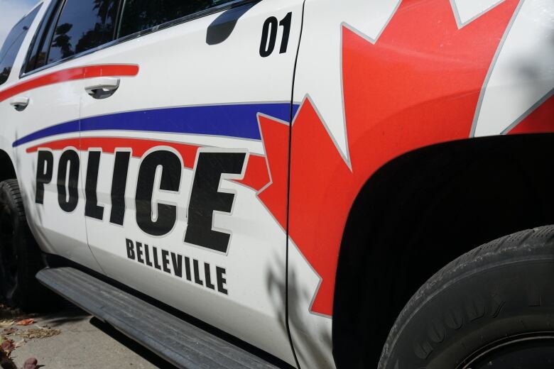 A close-up photo of the side of a white police car with a large maple leaf painted around the front wheel and the words 