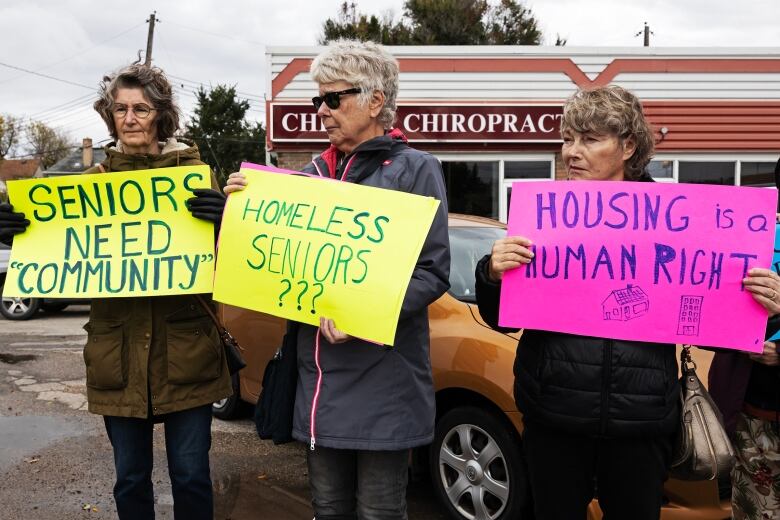 Three women hold three signs calling for the construction of more social housing.