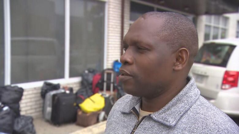 A man looks away from the camera. Luggage and a car can be seen behind him.