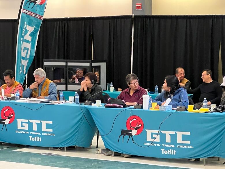 Four people sitting in a line behind a small table talk to one another.