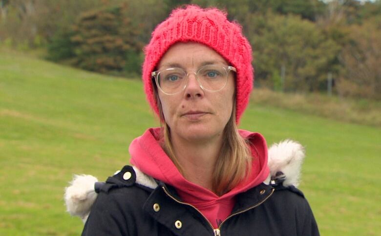 A woman wearing a pink hat and a black jacket standing on a grass lawn. 