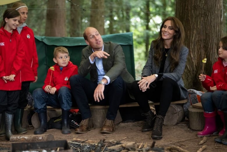 Adults and children sit and stand around a campfire pit.