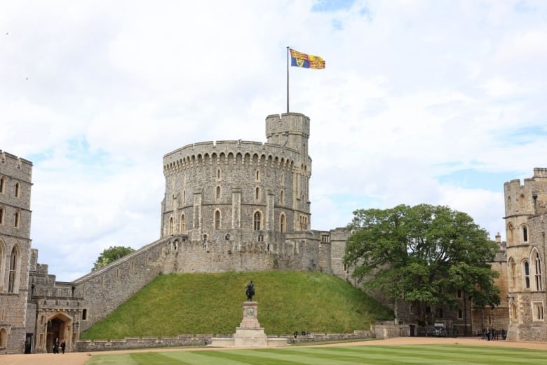 A flag flies from a pole above a round stone tower on a mound.