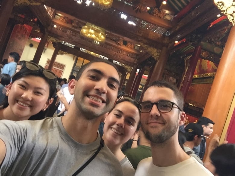 Selfie with four young adults smiling while inside a building with high ceilings and ornate columns.