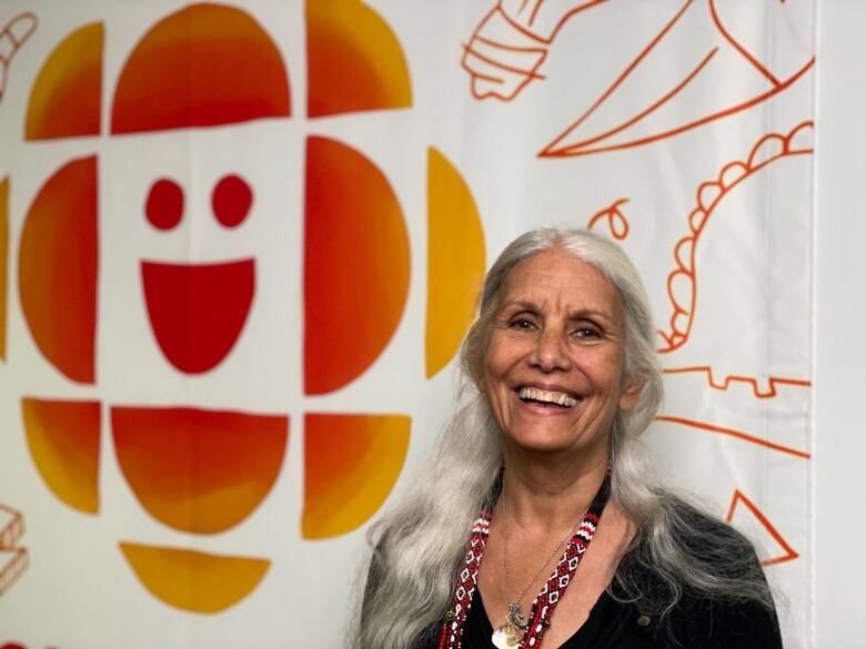 A smiling woman stands in front of the CBC logo on a wall. 