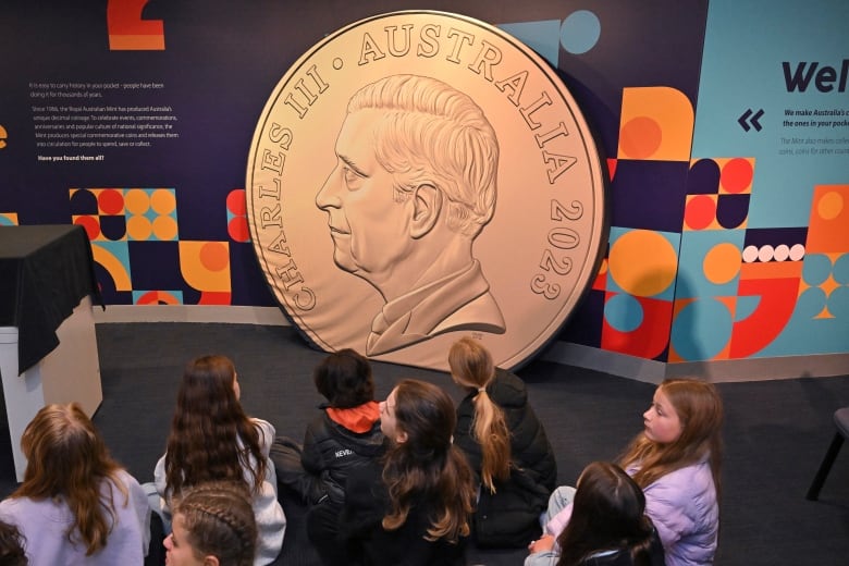 Schoolchildren sit in front of a mockup of a large coin.