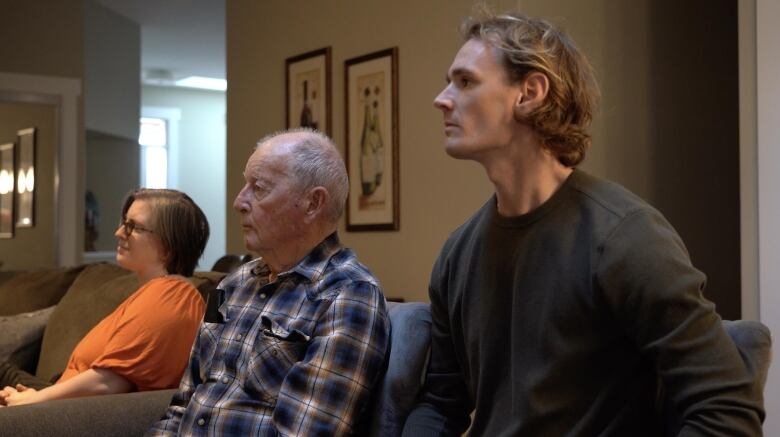 Three people sit in a living room, watching a documentary film.